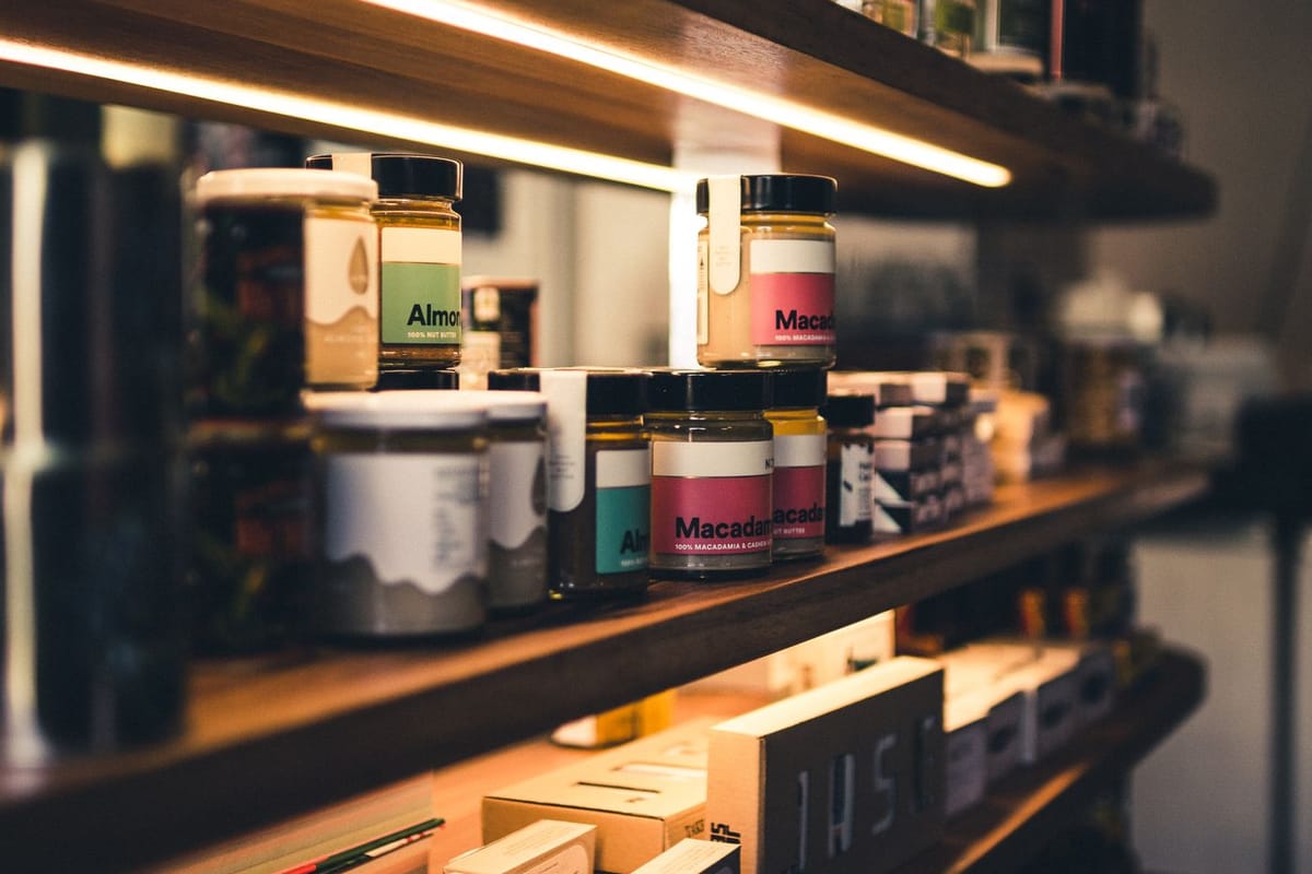 Jars of nut butter and preserves on the lit timber shelves of a speciality food retailer.