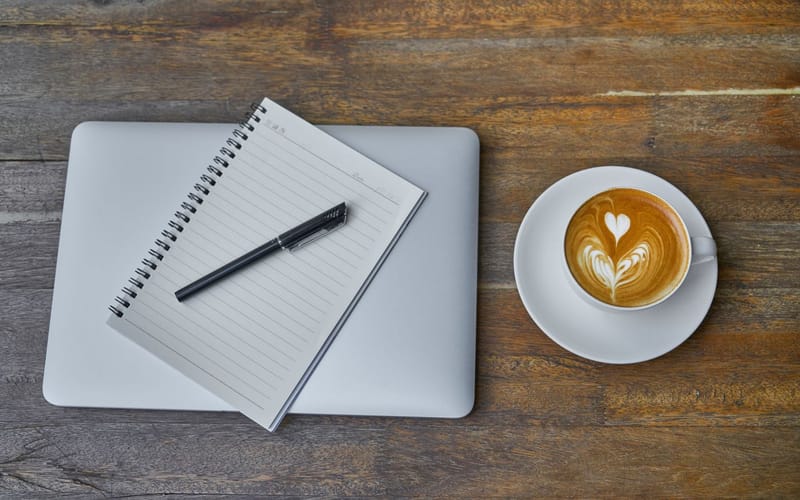 A laptop, open notebook and coffee on a desk, the correspondence an introduction begins with.